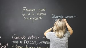 a blond child learning foreign language by writing it on a black board